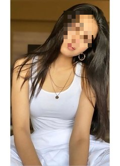 אדם לובש גופייה לבנה ועונד שרשרת עדינה ועגילים, יושב בחלל פנימי כששיערו הכהה פזור.