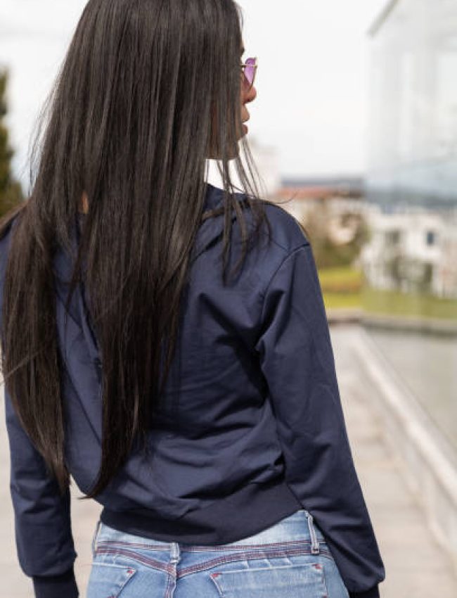 closeup of young latin woman with long, straight black hair posing on her back and standing in a casual jacket and jeans, wearing sunglasses, lifestyle and beauty