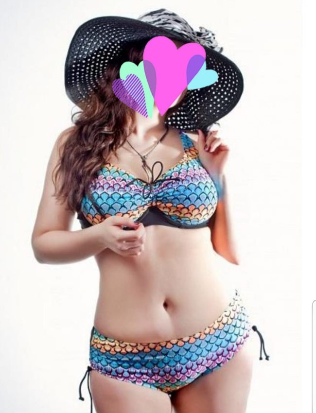 אישה לובשת בגד ים צבעוני עם דוגמת קשקשים וחובשת כובע רחב שוליים, כאשר פניה מכוסות בצורות לב.